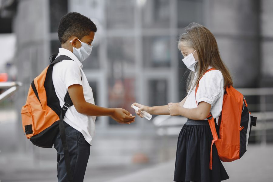 Niños con mochilas escolares y desinfectante